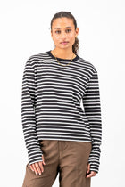 A woman modeling a black and white horizontally striped long-sleeve knit top with a crew neck, paired with brown pants, against a plain white studio background.
